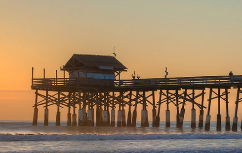 Picture of a wooden bridge that goes out onto the water with the sunset behind it.