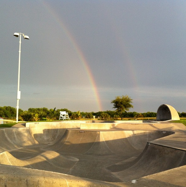 picture of a double rainbow in the sky behind the skatepark that people skate inside.