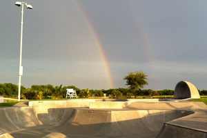 picture of a double rainbow in the sky behind the skatepark that people skate inside.