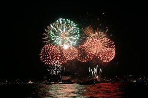 Picture of red and green fireworks blowing up in the night sky reflecting on the water below